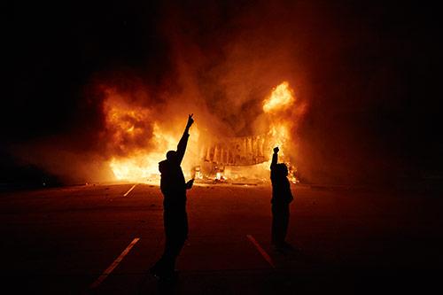 Onlookers stand on West Florissant Avenue as an AutoZone burns early Tuesday, Nov. 25, 2014 in Dellwood, Mo. A grand jury decided not to charge Ferguson police officer Darren Wilson in the fatal shooting of Michael Brown.<br/>