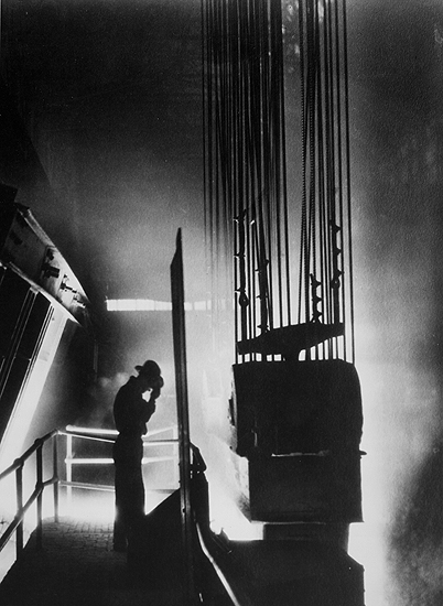 Ford Motor Company foreman shields his eyes against fiery light of open hearth mill, Detroit, MI 1929