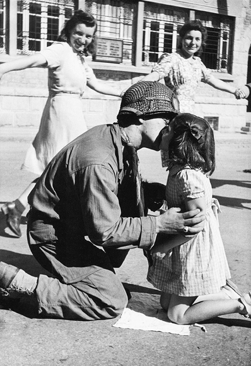 Kiss of Liberation: Sergeant Gene Costanzo kneels to kiss a little girl during spontaneous celebrations in the main square of the town of St. Briac, France, August 15, 1944