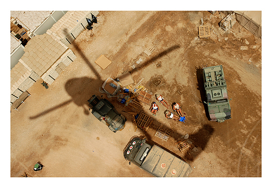 A Black Hawk helicopter carrying an American General momentarily blocks the sun of a group of Polish soldiers tanning themselves on a base in Karbala, Iraq on May 3, 2004