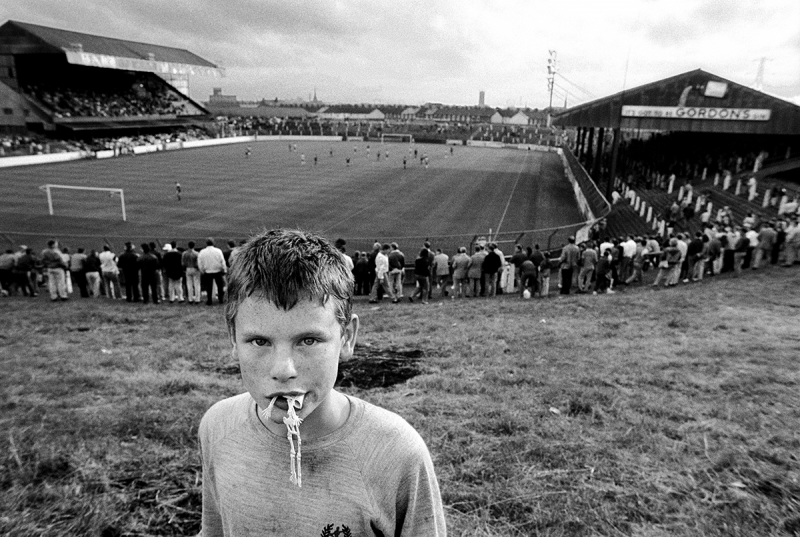 A young Protestant boy at a football game in Linfield Stadium in East Belfast. Northern Ireland, 1989 Archival Pigment Print