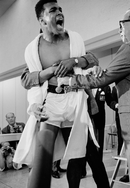 Cassius Clay (Muhammad Ali) restrained during weigh-in for Heavyweight Championship fight with Sonny Liston, Miami, 1964