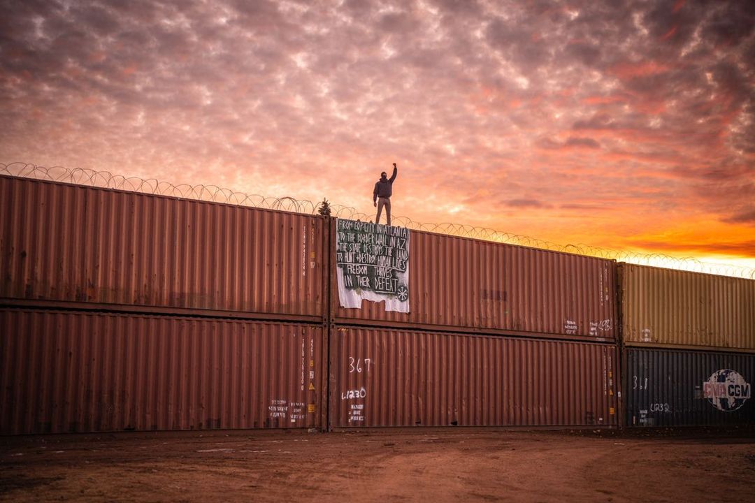 Protestor on illegal wall of shipping containers straddling the AZ / Mexico border , December, 2022
