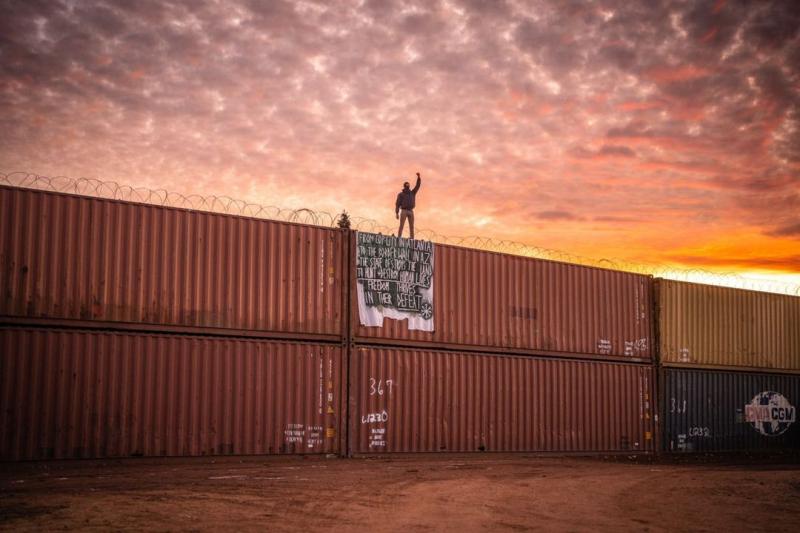 Ryan Vizzions Protestor on illegal wall of shipping containers straddling the AZ / Mexico border , December, 2022 Please contact Gallery for price