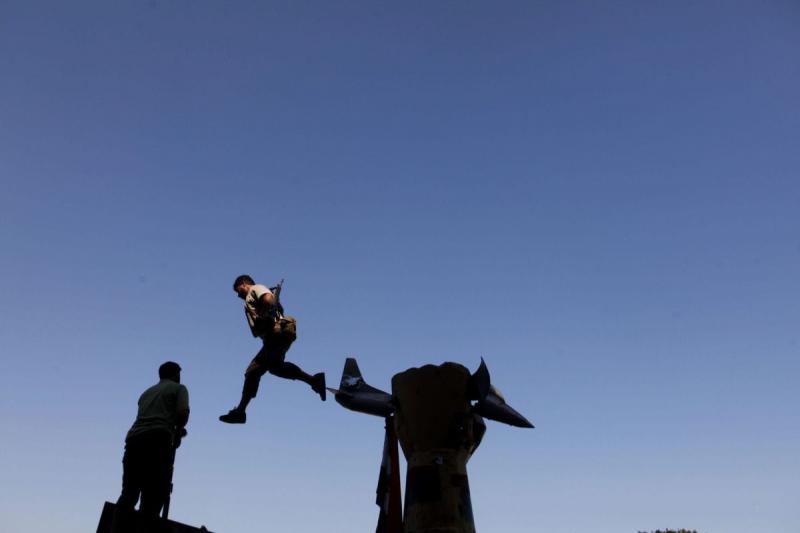Photo: A rebel soldier jumps off a statue of a fist crushing an American plane at Bab al-Aziziya, the  compound of Col. Muammar el-Qaddafi. Tripoli, Libya, 2011 Archival Pigment Print #2960
