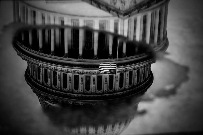 black and white photograph of The US Capitol with American Flag reflected in a puddle of water on the ground, Washington, DC, January 3, 2021
