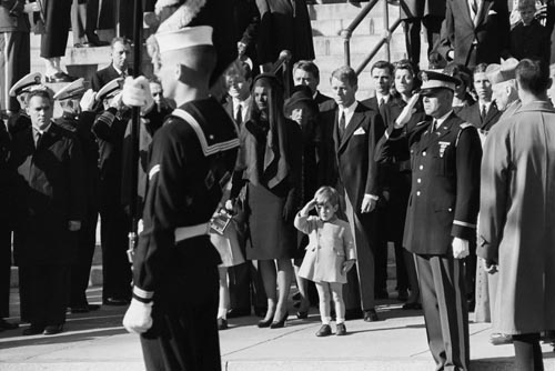 John F. Kennedy Jr. saluting his father's coffin, November 25, 1963 with Ted Kennedy, Jacqueline Kennedy, Rose Kennedy, Peter Lawford, and Robert F. Kennedy in background.